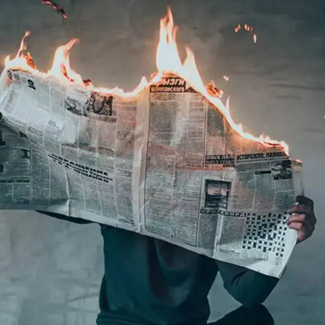 A person holding a newspaper on fire